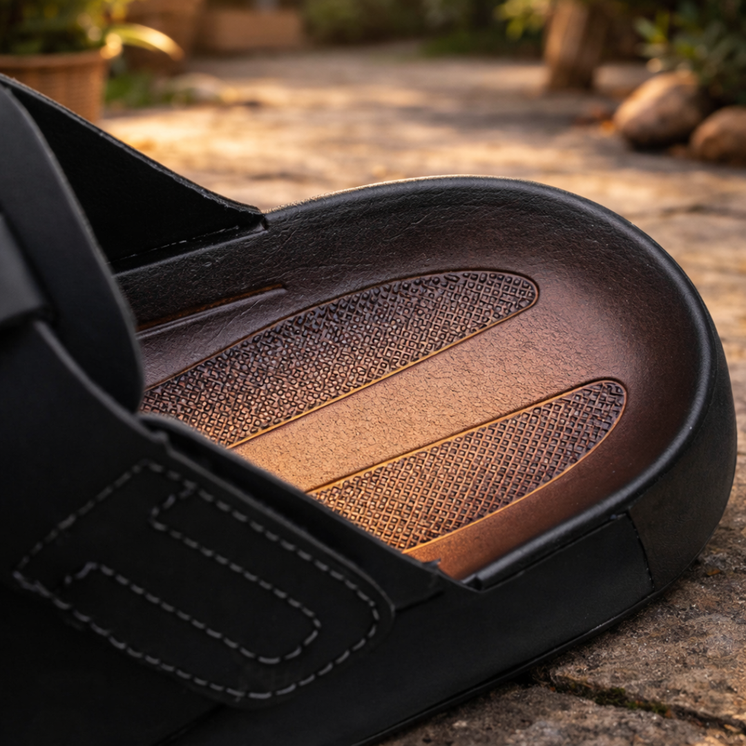 Close-up of a black sandal with brown insole on a stone surface.